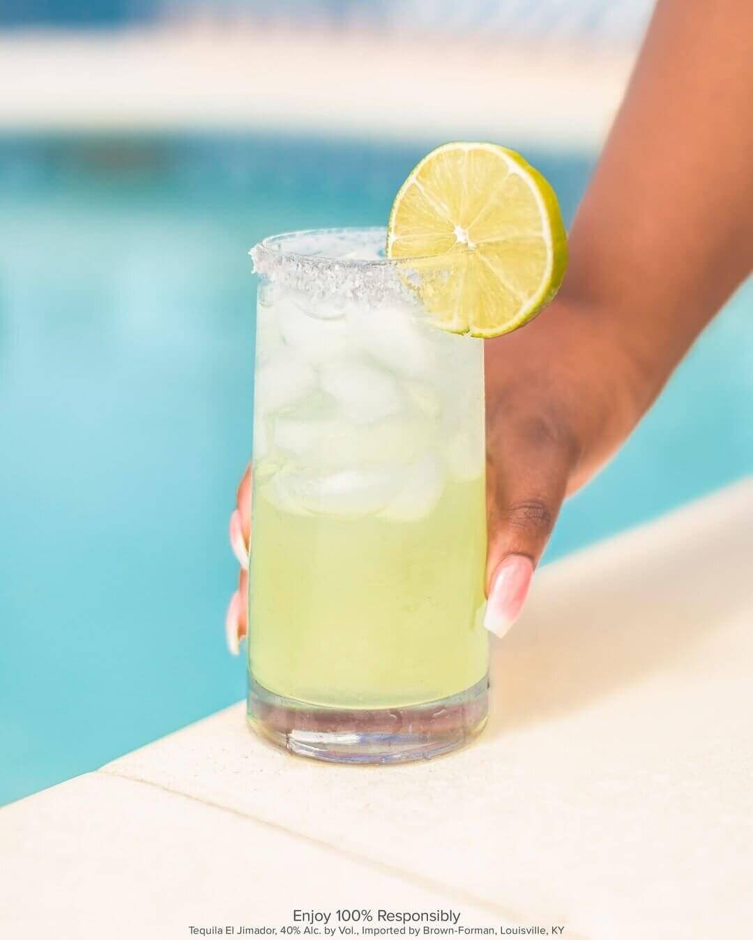 Close-up photo of woman's hand holding margarita near the edge of a pool 