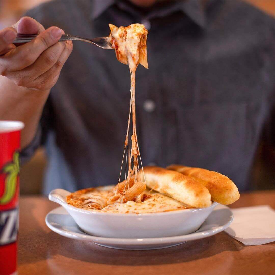 Freeze-frame photo of melty cheese stretching from pasta plate to man's fork 