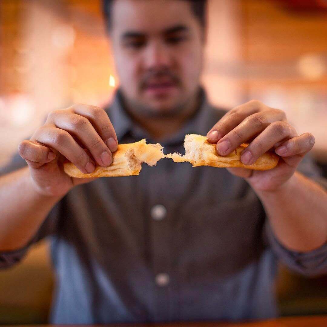 Close-up freeze-frame photo of man ripping a breadstick in two 