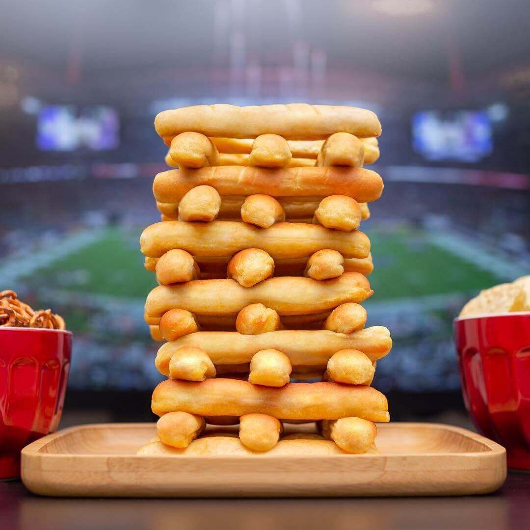 Tall stack of breadsticks arranged like Jenga blocks in front of a TV with the Super Bowl on 