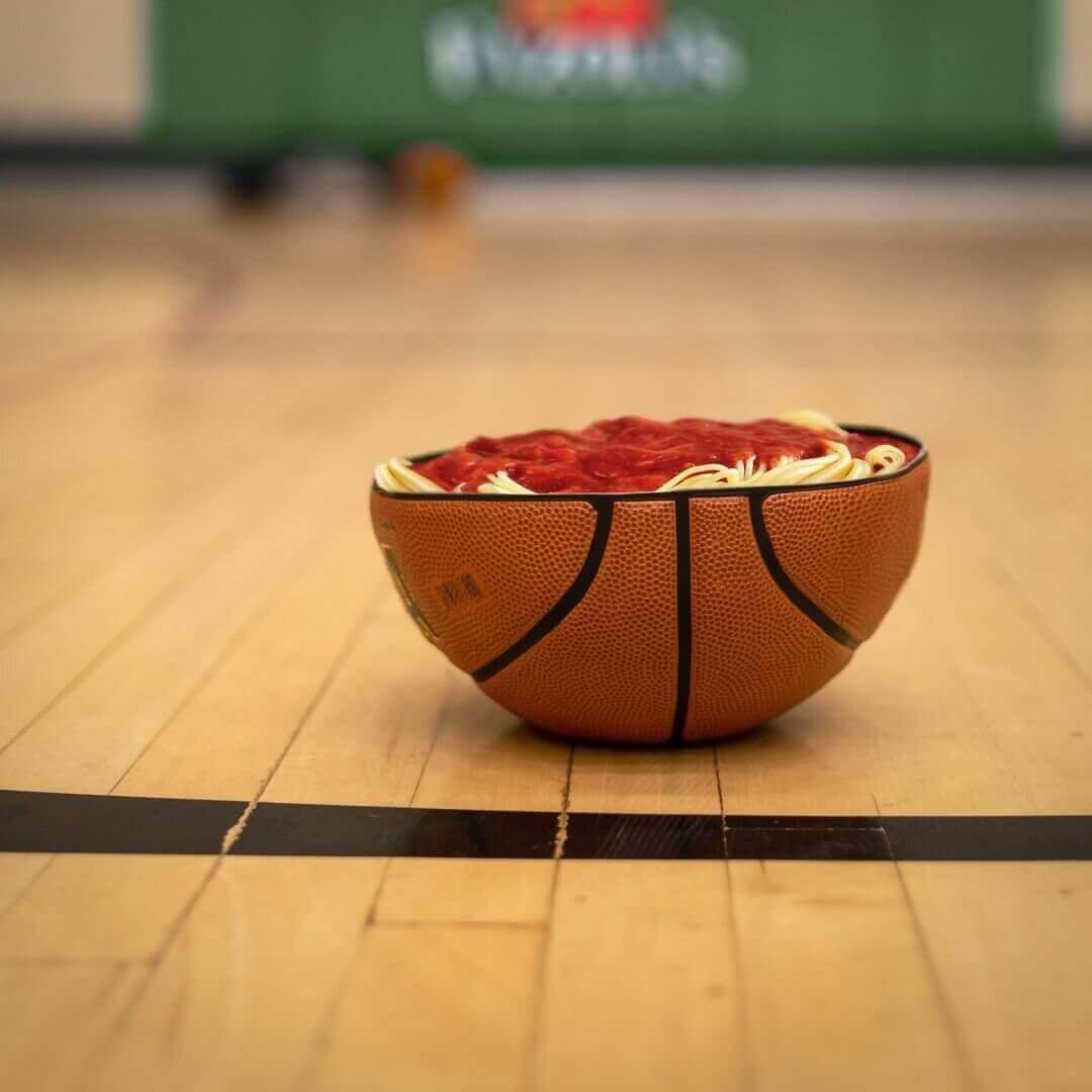 Bowl-shaped lower half of a basketball is filled with spaghetti and sitting on a basketball court 
