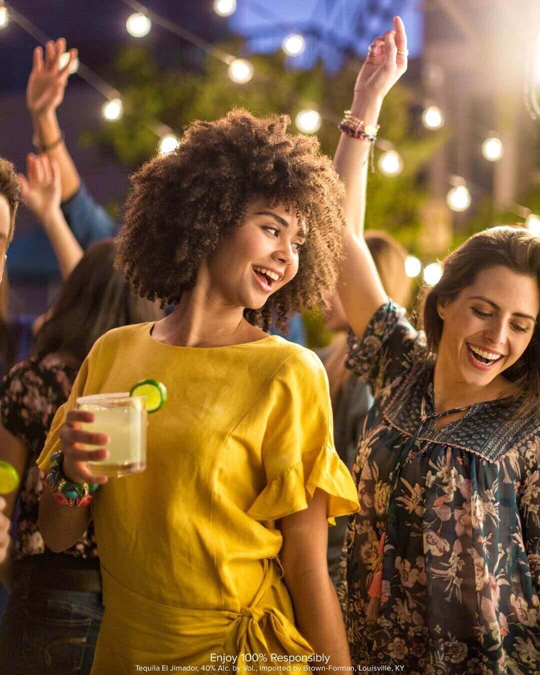 Two women dancing in a crowd with margaritas in their hands 